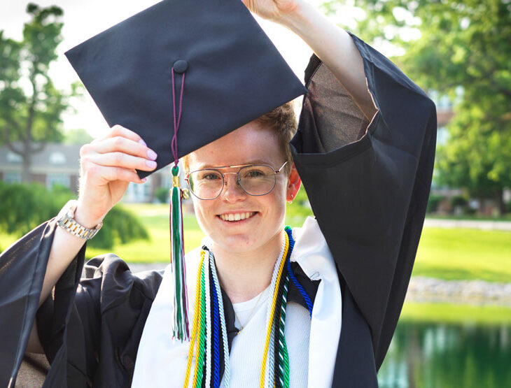 Aurora Lucie Henriksen in her graduation cap and gown near Senior Lake on campus