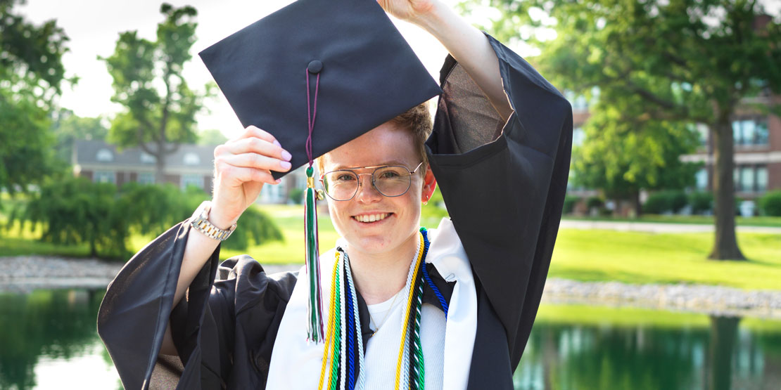 Aurora Lucie Henriksen in her graduation cap and gown near Senior Lake on campus