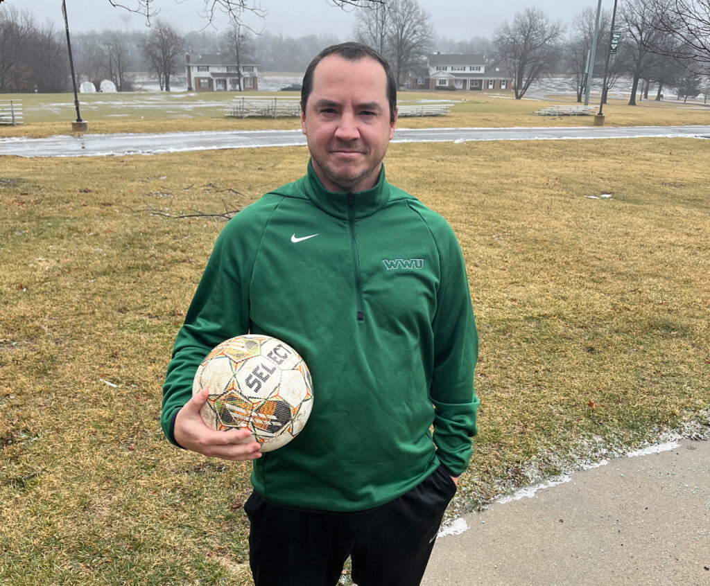 Men's Soccer Coach Tommy Nienhaus poses with a soccer ball